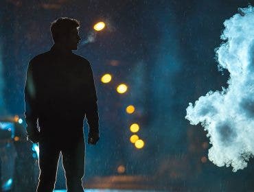 man standing in the street under the rain during night time