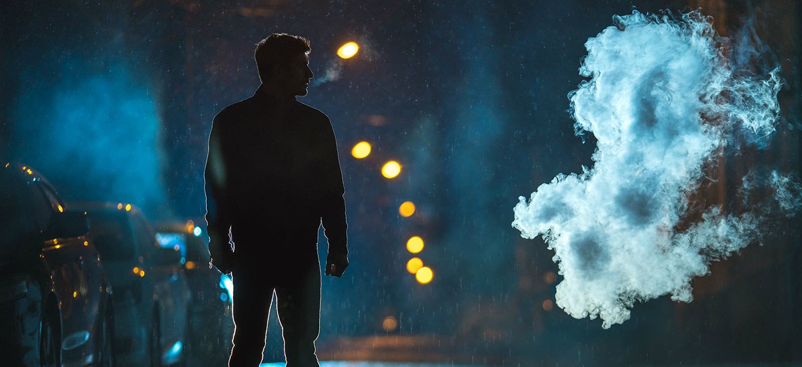 man standing in the street under the rain during night time