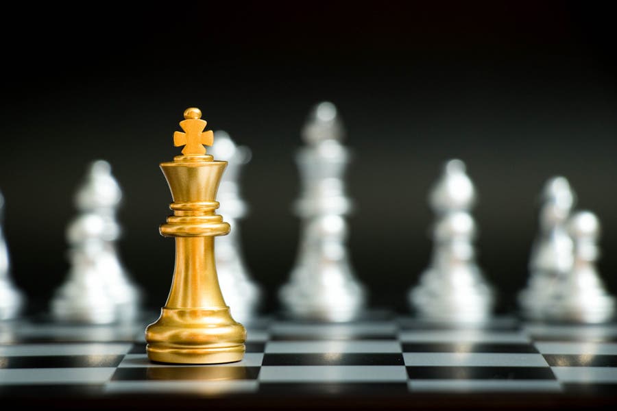 Gold king chess piece with silver chess pieces in background bokeh