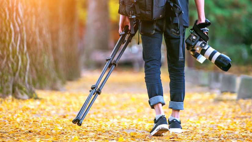 Professional photographer with camera and tripod in autumn.