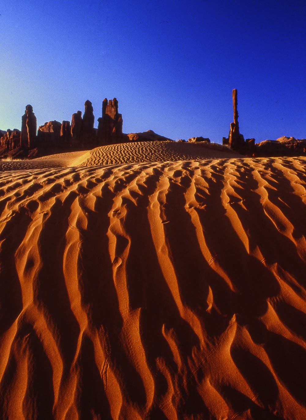 Here I combined the rippled sand dunes in the foreground with the needle-like rock formations further back into a simple abstract composition based on two color blocks: earth and sky. Shot in Monument Valley with a moderate wide-angle lens (35mm) at dawn and polarized to deepen the blue of the sky.