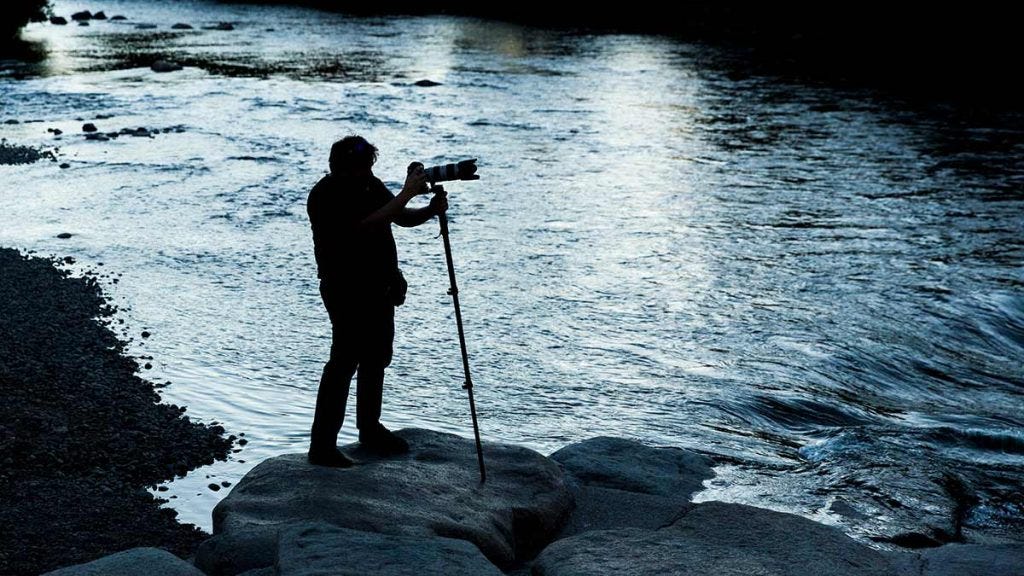 fotógrafo con cámara monopie haciendo fotografía de paisajes en el lago