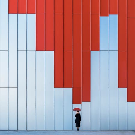 woman holding red umbrella in front of wall with red paint