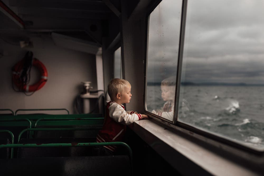 young boy watching the water while inside a ferry boat