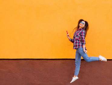 Cheerful girl mid jump against colored wall
