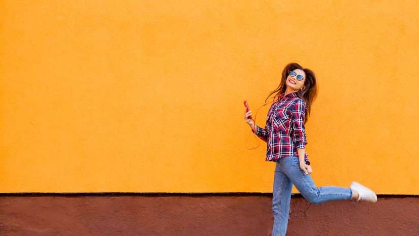 Cheerful girl mid jump against colored wall