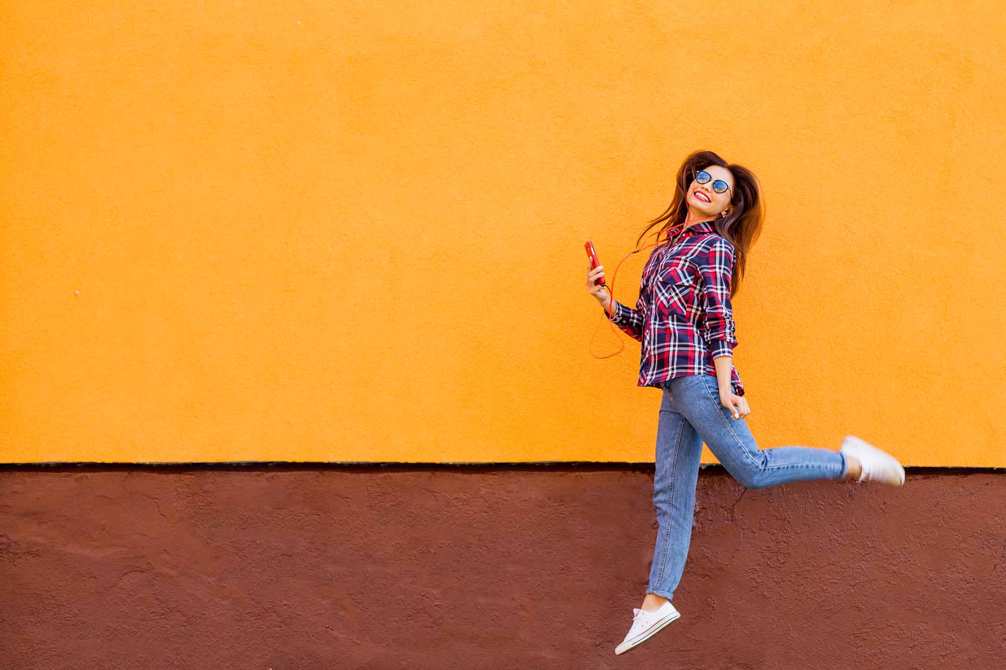 Cheerful girl mid jump against colored wall
