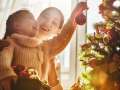 mother helping daughter hang Christmas tree decorations