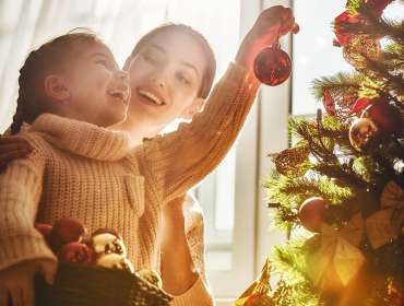 mother helping daughter hang Christmas tree decorations