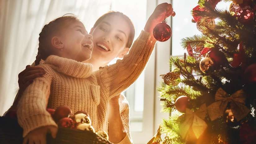 mother helping daughter hang Christmas tree decorations