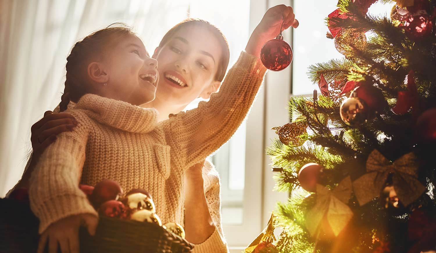 mother helping daughter hang Christmas tree decorations
