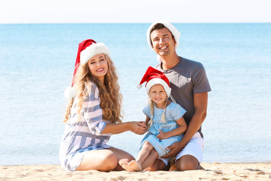 family Christmas photo shoot of family wearing santa hats on the beach