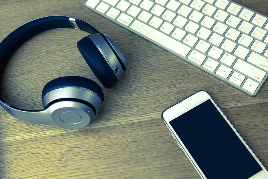 iphone, imac keyboard, and headphones on wooden table