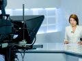 female TV anchor sitting in front of camera and teleprompter