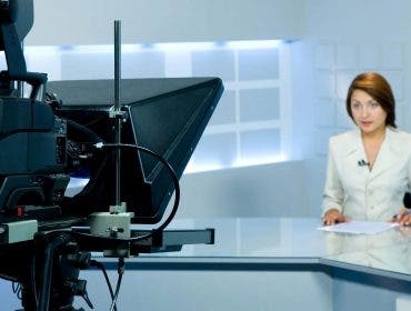 female TV anchor sitting in front of camera and teleprompter