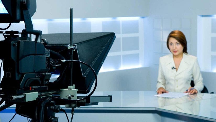 female TV anchor sitting in front of camera and teleprompter