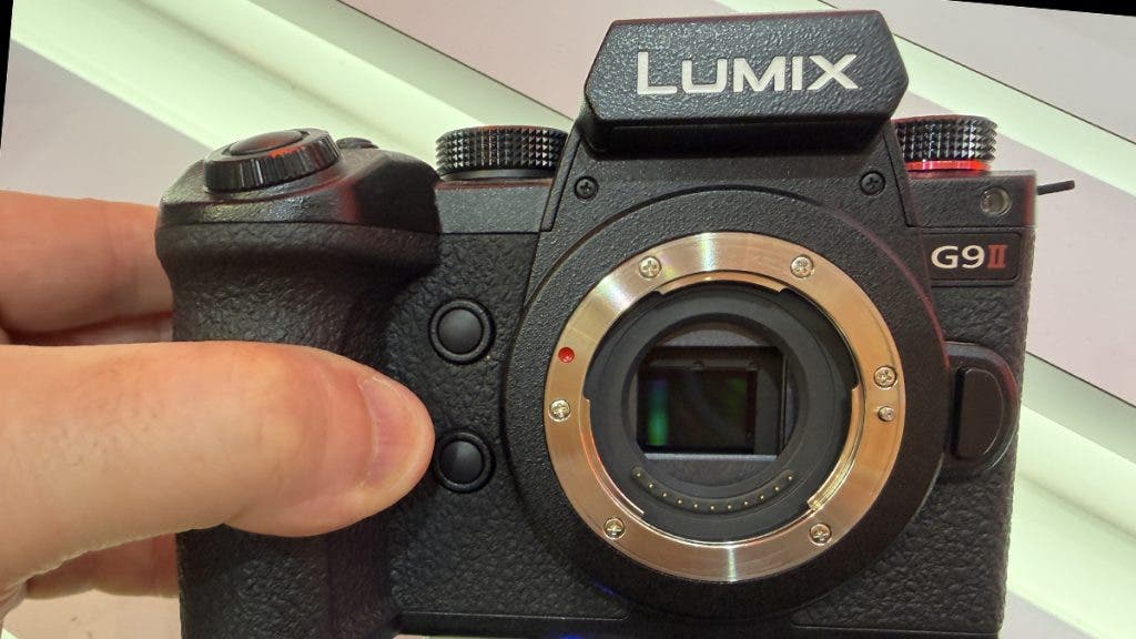 A hand holding a black Panasonic Lumix G9II mirrorless camera with the lens removed, showcasing the square-like Micro Four Thirds (MFT) camera sensor size inside the lens mount.