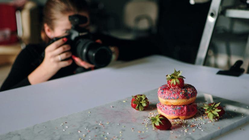 food photographer photographing pink donuts on table with professional camera