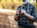 best binoculars for birding, man birdwatching with binoculars in nature forest