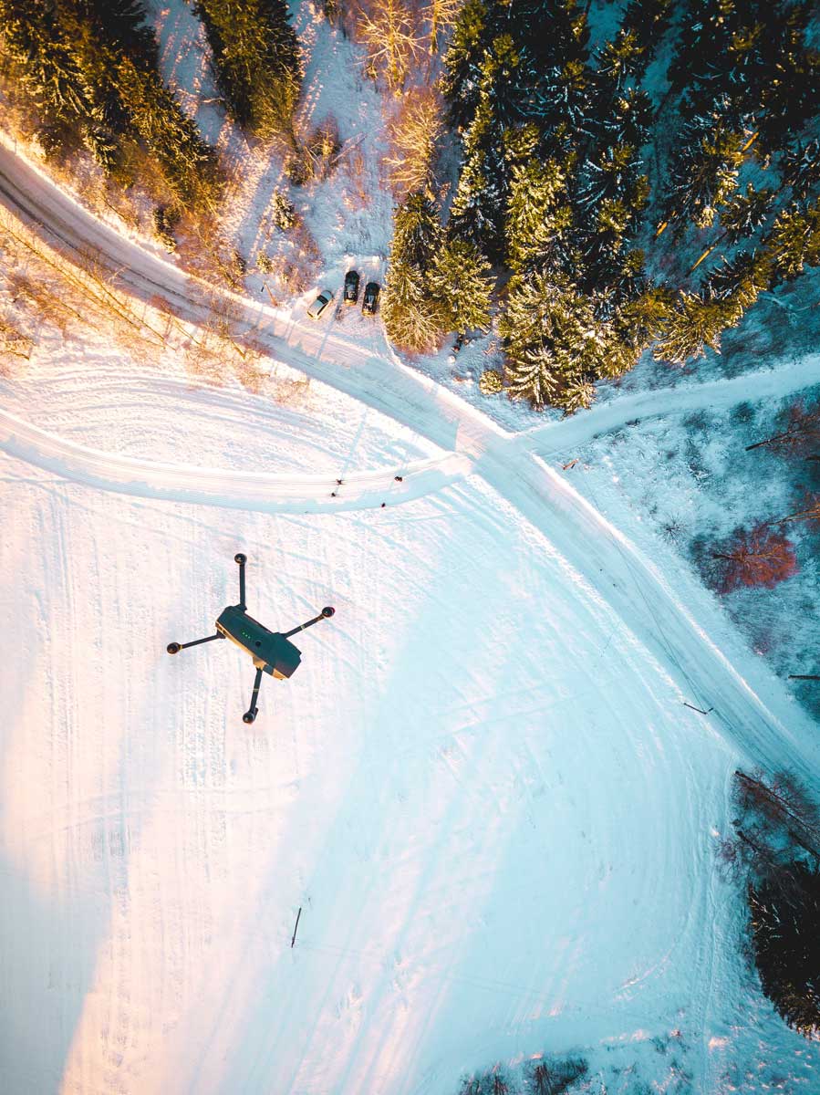 drone flying over winter landscape with snow, trees, and car