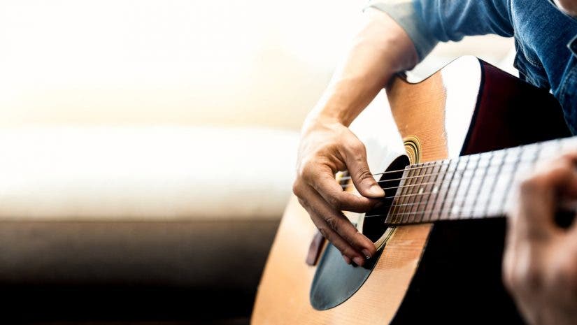 man playing acoustic guitar strings