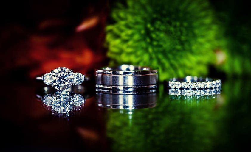 Wedding rings in front of a bouquet on a reflective surface