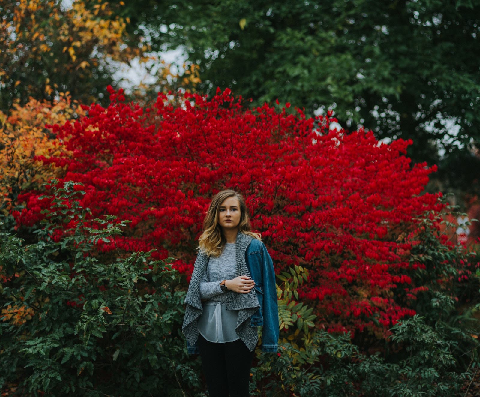girl in jacket stands in front of bushes