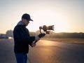 Man filming with camera and gimbal against city at sunrise