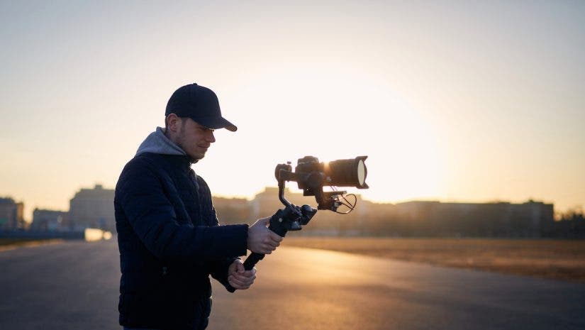 Man filming with camera and gimbal against city at sunrise
