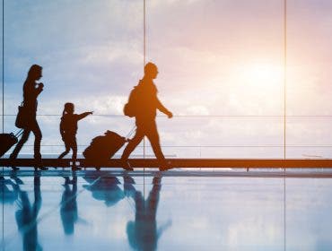 Family at airport travelling with young child and luggage walking to departure gate, girl pointing at airplanes through window, silhouette of people, abstract international air travel concept