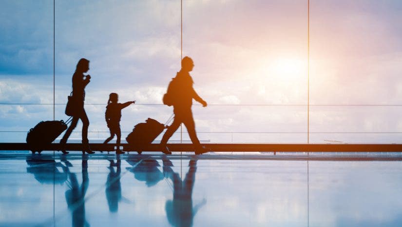 Family at airport travelling with young child and luggage walking to departure gate, girl pointing at airplanes through window, silhouette of people, abstract international air travel concept