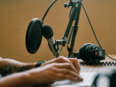 Man working on keyboard editing a podcast with headphones and a microphone in the background