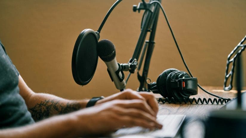 Man working on keyboard editing a podcast with headphones and a microphone in the background