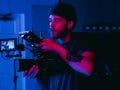 Videographer filming a scene, lit dramatically with purple and blue light