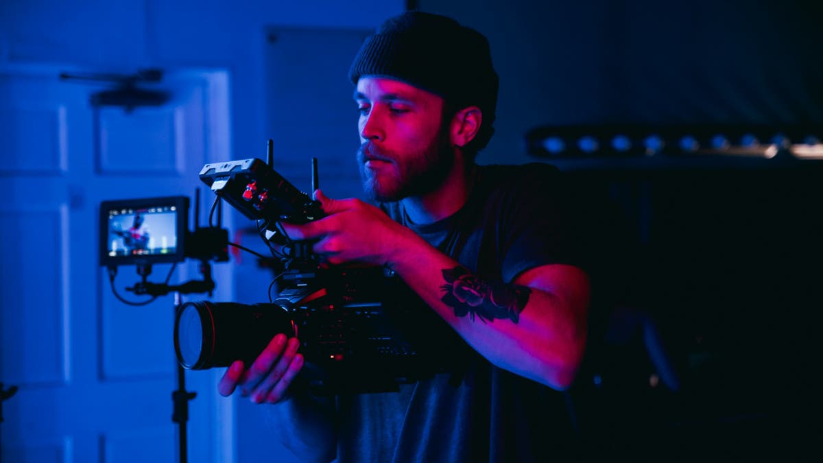 Videographer filming a scene, lit dramatically with purple and blue light