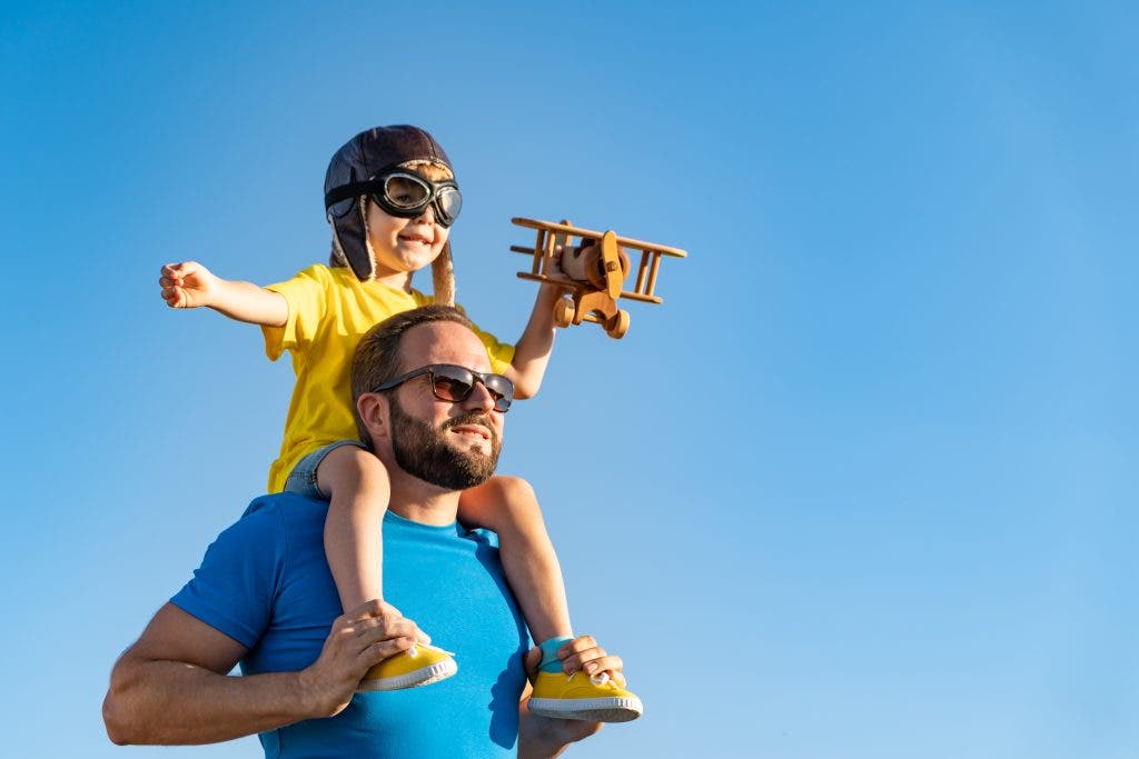 Happy family having fun outdoor. Father and son playing against blue summer sky background. Imagination and freedom concept