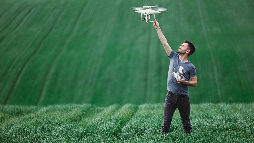 Man-holding-drone-before-flight-in-field-adobe-stock