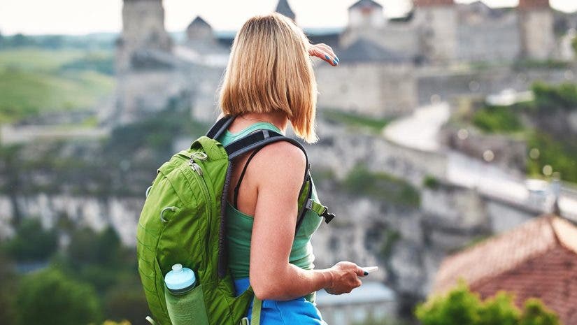 Woman tourist with green backpack makes a photo of an old castle. vacation and summer trip