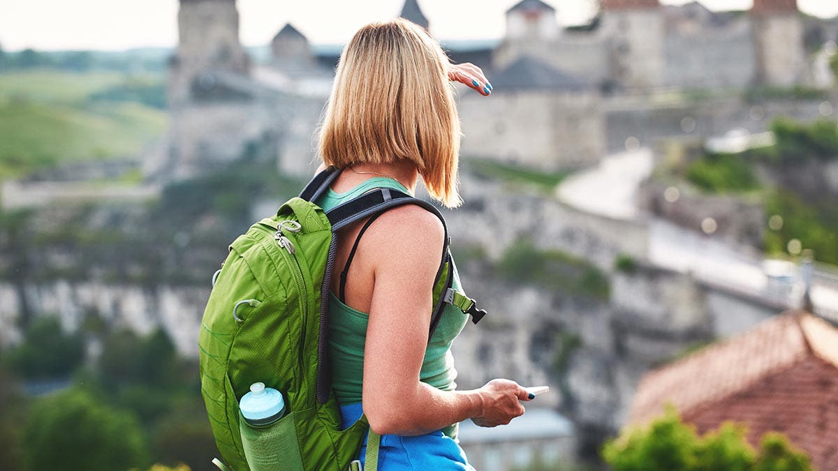 Woman tourist with green backpack makes a photo of an old castle. vacation and summer trip