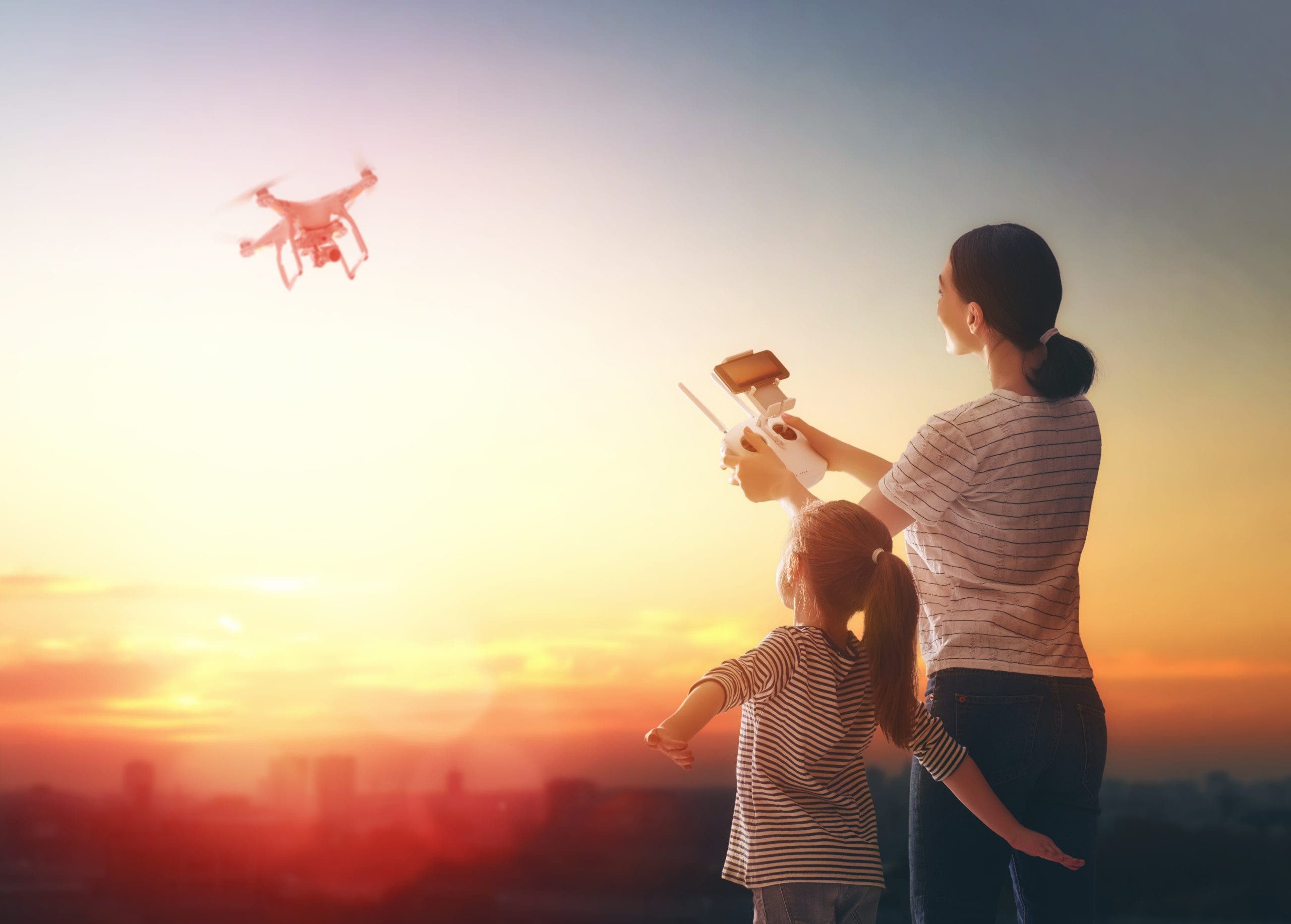 Little girl and her mother are operating the drone by remote control in the park. Kid and mom are playing with quadrocopter outdoors.
