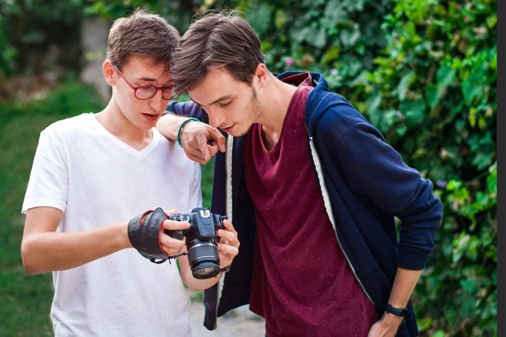 Young man photographer having a conversation with the model. Showing the camera. Green forest on background