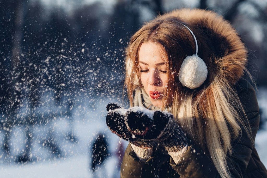 a photo of a woman wearing winter protection in cold weather blowing snow off her hands