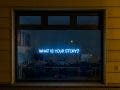 a neon light that says "what is your story?"