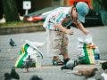 a boy in public picking up trash while surrounded by pigeons