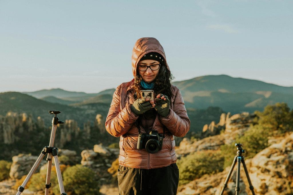 a photographer standing on top of a mountain playing with her phone