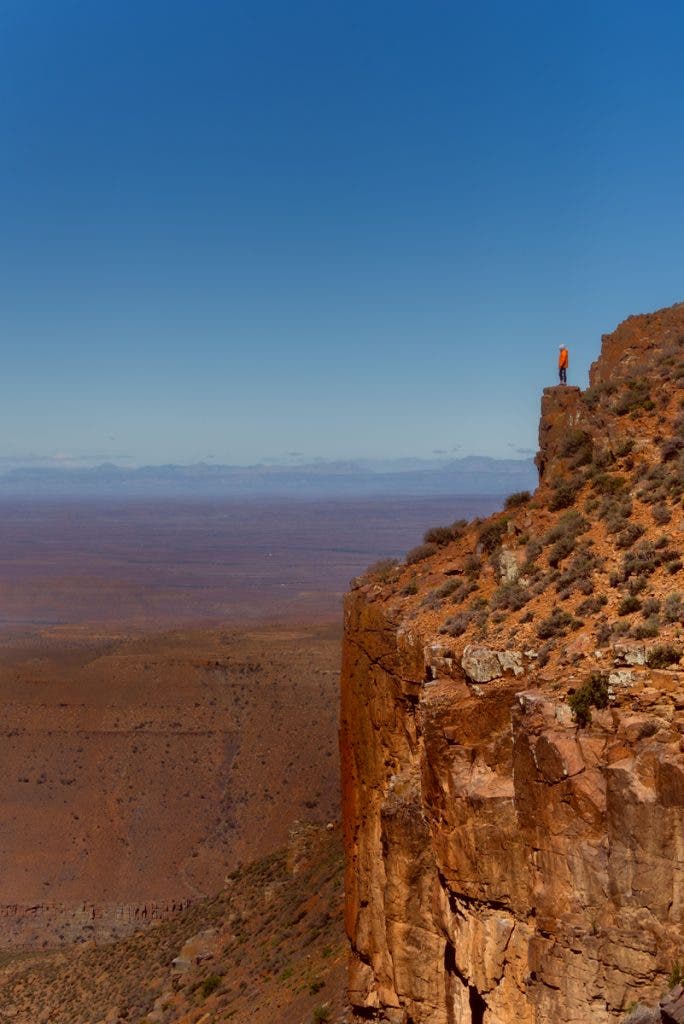 Sometimes, the subject is also the anchor. From the semi-desert region of Roggeveld, the subject of this image is the individual standing at the cliff's edge. His vivid orange jacket contrasts sharply with the earthy colors of the surroundings, bright against the blue sky, capturing attention instantly. Because of his small stature in relation to the expansive landscape as the sole pop of bright color, the person serves as the subject and the key anchor, too.