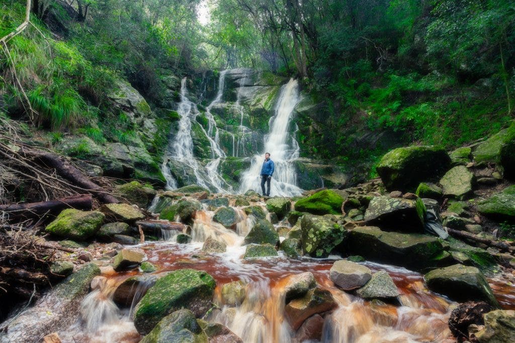 The slow shutter speed creates a motion blur of the waterfall, enhancing the focus on the subject: the man standing on the rock. A fast shutter speed would have shown the water in sharp detail, creating a distraction