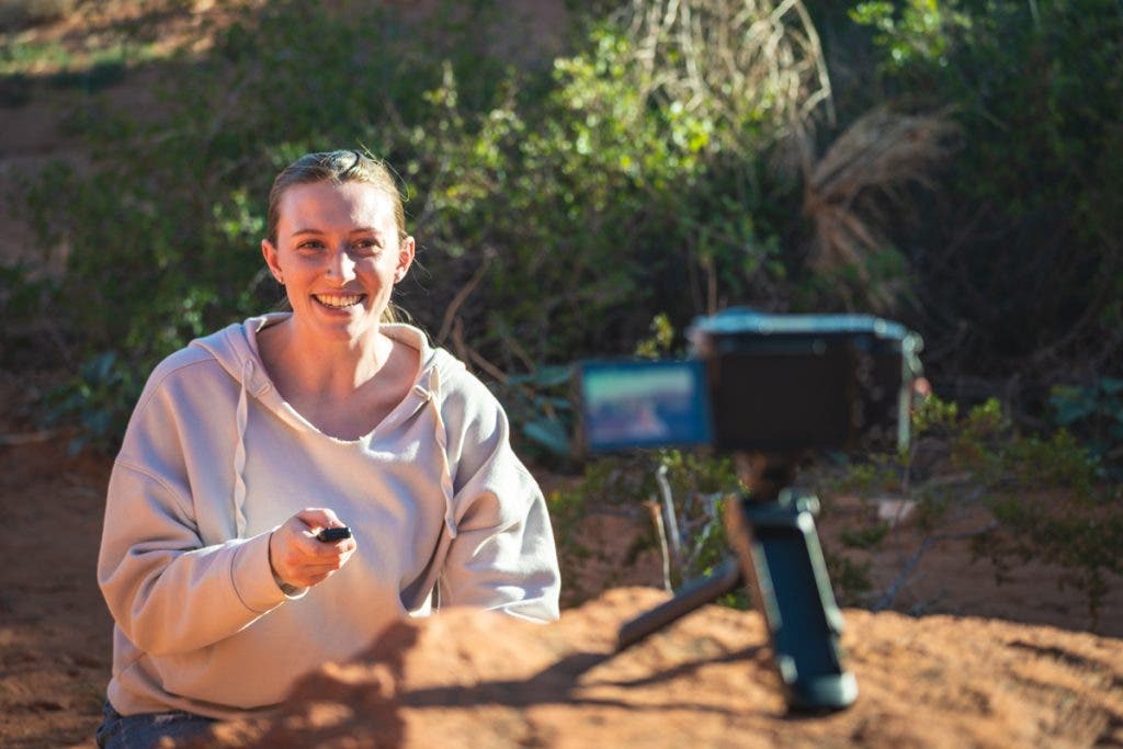 The Sony GP-VPT3 Remote Control female subject recording a video with a camera mounted on a tripod and the remote in hand