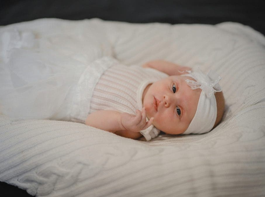 a newborn baby lying on the bed wearing white and a ribbon on the head