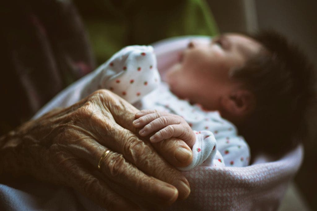 newborn photograph of baby sleeping next to grandma holding its hand
